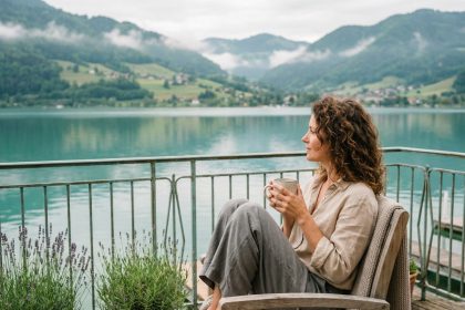 Femme savourant un café sur la terrasse en bois d'un hôtel face au lac d'Annecy, avec vue panoramique sur les montagnes alpines